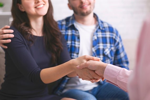 woman shaking hands while partner has arm on her shoulder